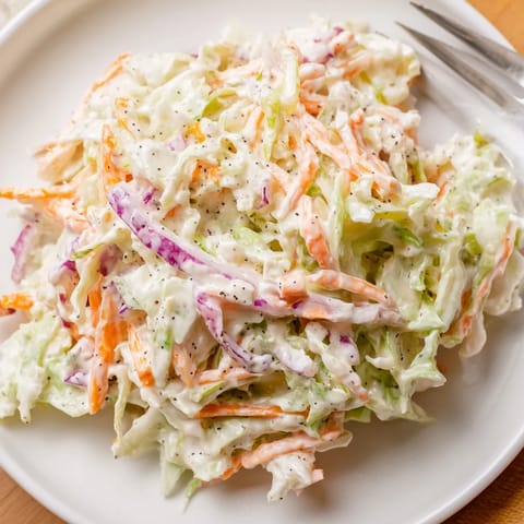 Creamy Coleslaw served chilled in a white bowl, featuring crunchy vegetables and a hint of Dijon mustard for flavor.
