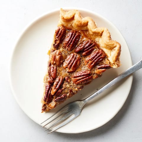 Slice of Southern Pecan Pie on a white plate, topped with whipped cream and drizzled with caramel sauce.