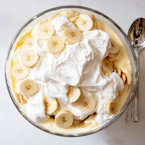 Creamy banana pudding layered with vanilla wafers and fresh slices, topped with fluffy whipped cream in a glass dish.