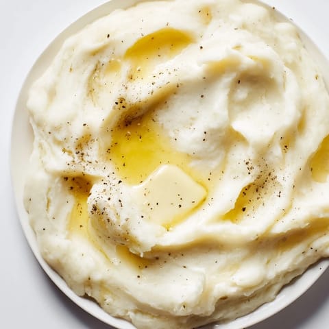 Freshly made Mashed Potatoes topped with chopped chives in a rustic white bowl, a classic American side.