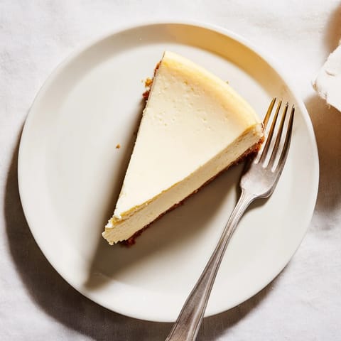 Freshly baked New York cheesecake with a golden graham cracker crust, served warm on a dessert plate.