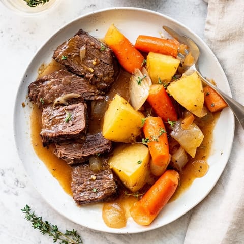 A steaming hot Beef Pot Roast served in a rustic Dutch oven, with onions and carrots simmering in savory juices.