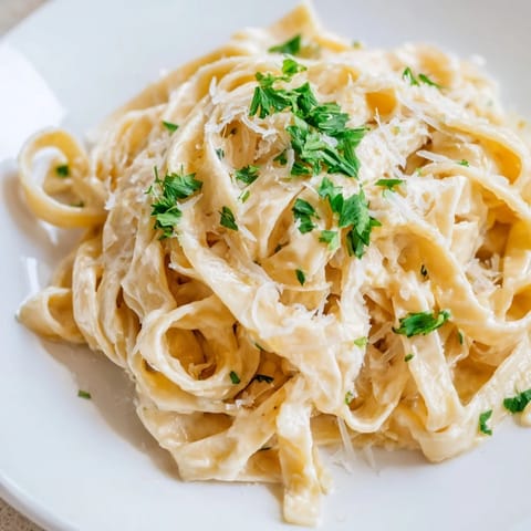 Creamy roasted garlic pasta garnished with fresh parsley and grated Parmesan on a rustic wooden table.  
