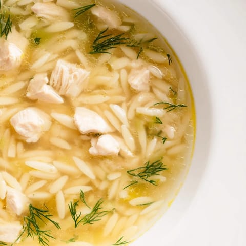 Comforting Mediterranean Chicken Lemon Orzo Soup served in a rustic bowl with fresh dill and lemon wedges.  