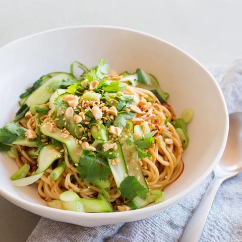 A vibrant Spicy Sesame Noodle Salad served in a bowl, topped with chopped spring onions and roasted peanuts for crunch.  