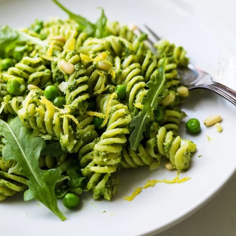 Plate of Spring Green Pesto Pasta Salad topped with crumbled feta cheese, extra pine nuts, and fresh herbs for a delicious spring meal.
