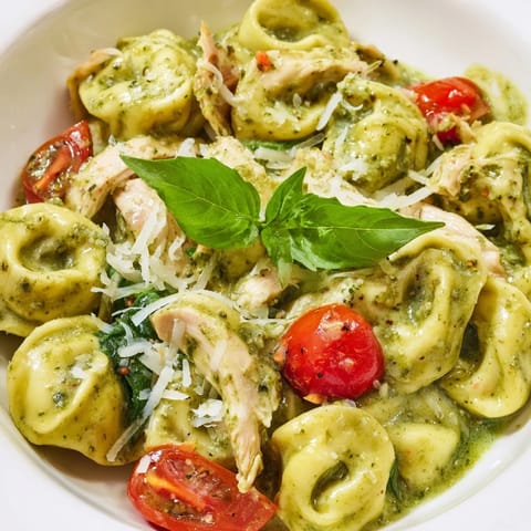 Savory Creamy Pesto Tortellini Skillet featuring juicy chicken pieces and halved cherry tomatoes nestled in a rich, bubbling Parmesan cream sauce.