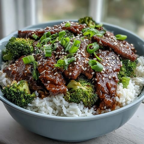 A steaming Beef and Broccoli Bowl features tender beef strips, fluffy white rice, and bright green broccoli florets tossed in a glossy sauce.