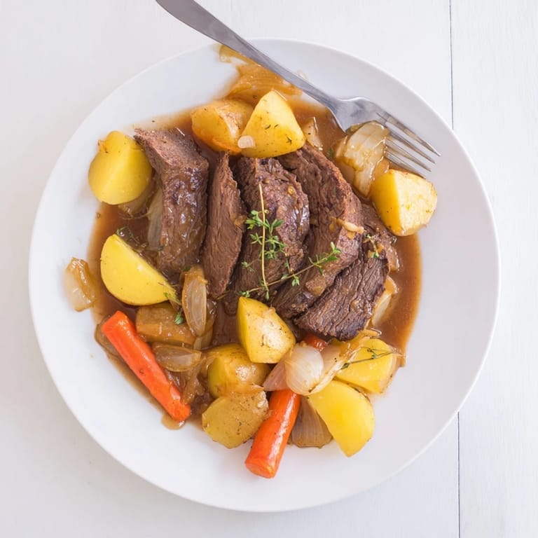 Sliced Beef Pot Roast plated alongside glazed carrots, Yukon Gold potatoes, and a ladle of thick, peppery gravy.