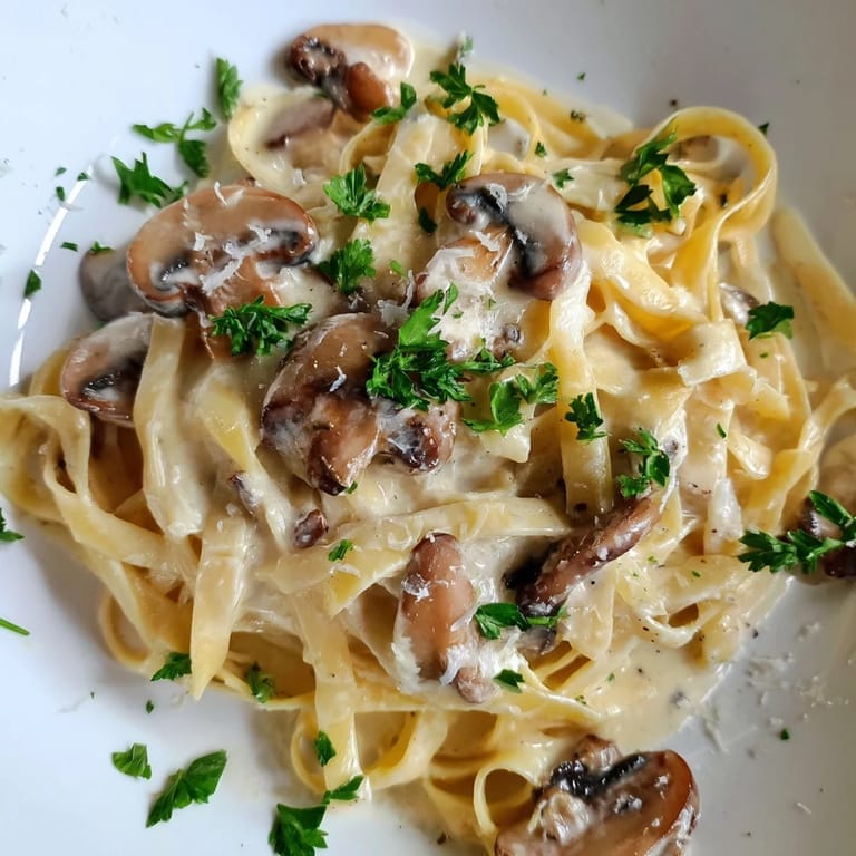 Close-up of Creamy Mushroom Alfredo showing tender mushrooms, garlic flecks, and silky sauce clinging to every strand of pasta.