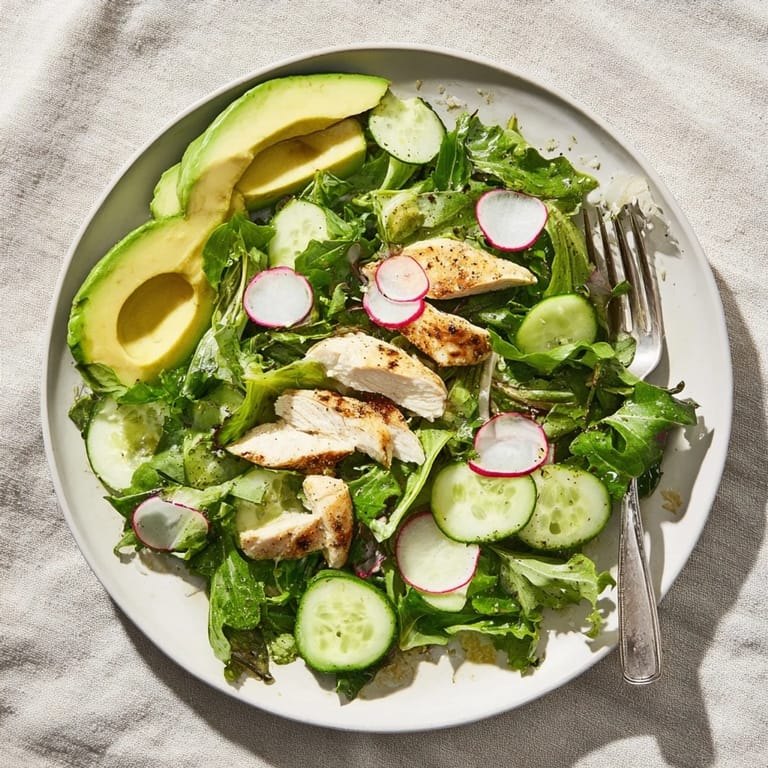 A close-up of the Spring Detox Chicken Salad reveals tender, golden-brown grilled chicken nestled among vibrant spinach and arugula leaves, with thin slices of cucumber and radish adding crunch. A glistening lemon vinaigrette coats every ingredient, making it an irresistible and healthy low-carb meal.