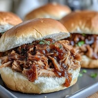 Golden-brown shredded Applesauce Pulled Pork Sandwiches piled high on toasted buns, garnished with fresh coleslaw for a sweet and savory bite.