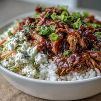 Fluffy white rice topped with slow-cooked pulled pork and tangy coleslaw in a rustic ceramic bowl.