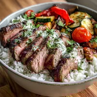 A bowl of Grilled Steak Bowl with fluffy rice and colorful roasted vegetables.